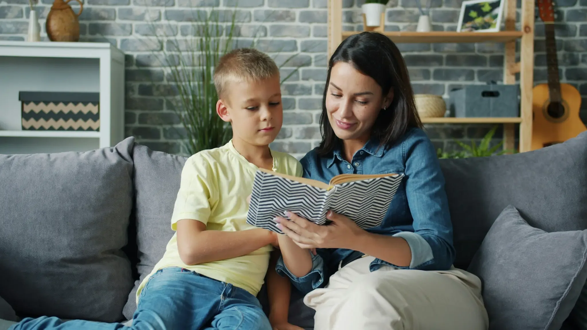 Mutter liest ihrem Sohn auf dem Sofa ein Buch vor